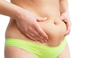 Attractive woman with bare midriff holding extras sking around her waist - Liposuction candidate